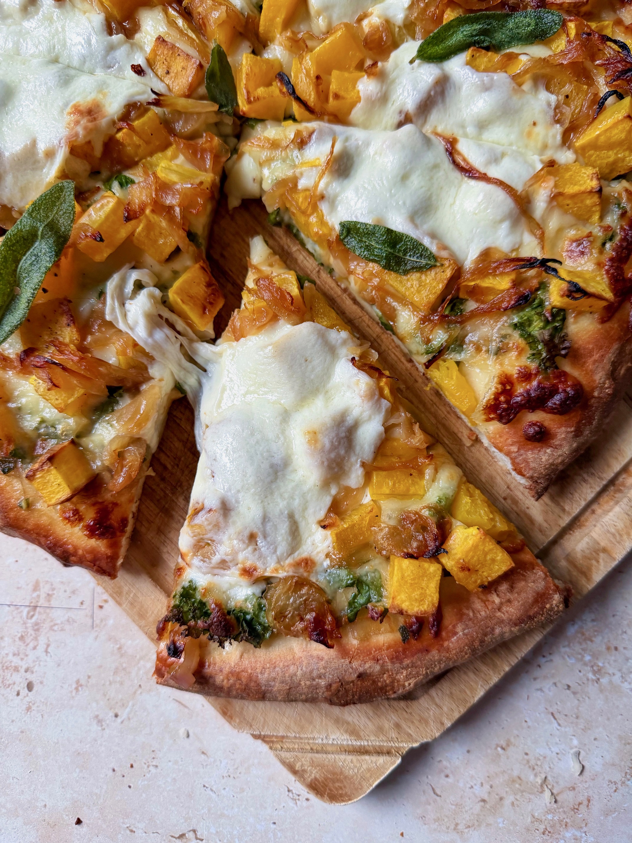 A slice of butternut squash pizza with a cheese pull.